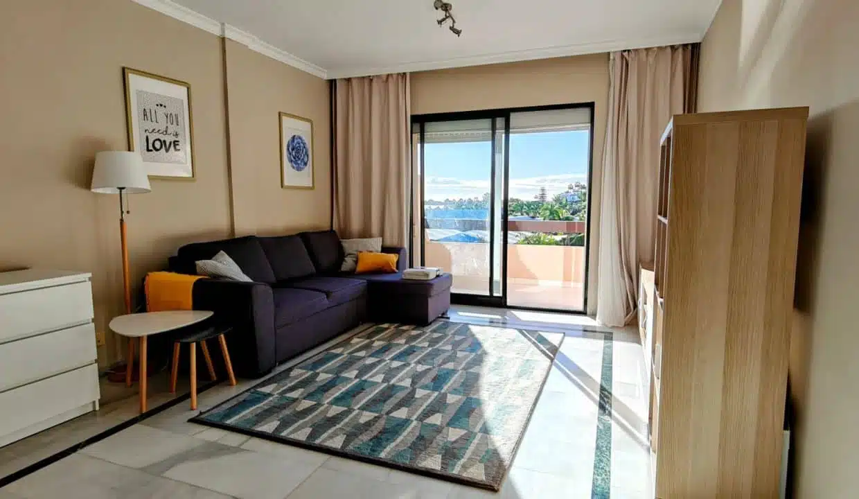 Salon avec canapé gris foncé, tapis bleu et accès terrasse – appartement à louer, Las Terrazas de Bel Air, Estepona