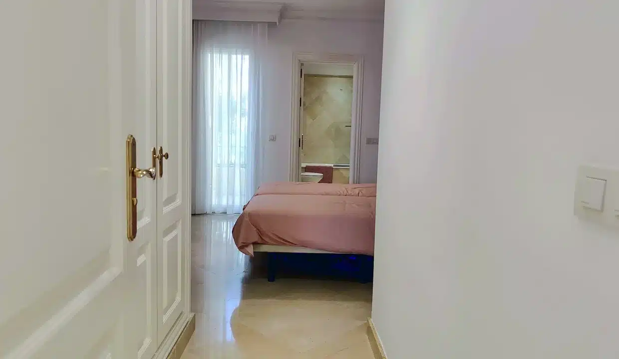 Dormitorio con colcha rosa, visillos y baño al fondo – apartamento en alquiler, Majestic Hills, Casares (ref. AL014)