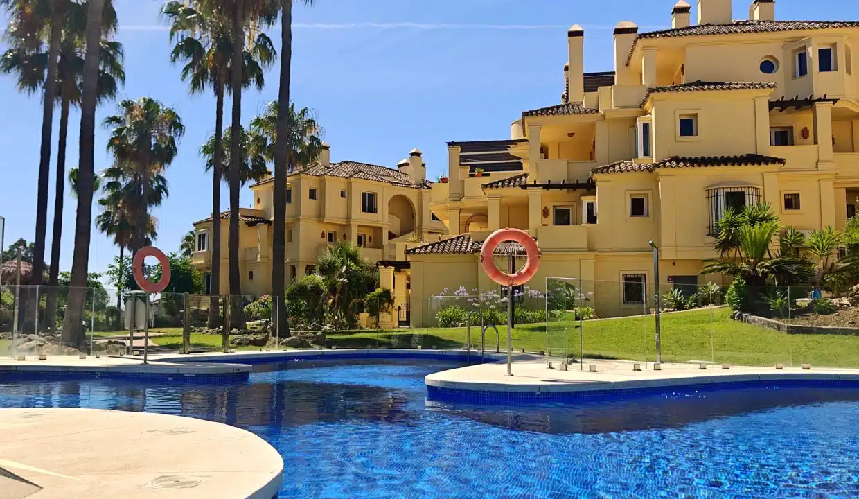 Piscina comunitaria con residencia ocre de tejas y palmeras – apartamento en alquiler, Majestic Hills, Casares (ref. AL014)