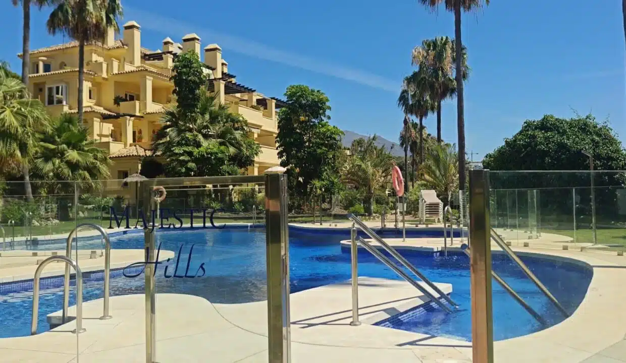 Piscina comunitaria tras una valla de cristal, edificio ocre – apartamento en alquiler, Majestic Hills, Casares (ref. AL014)