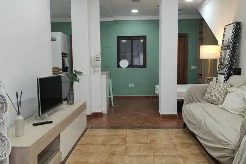 Studio living area with beige sofa, light TV unit and bed at the back – studio for rent, Estepona town centre (ref. AL012B)