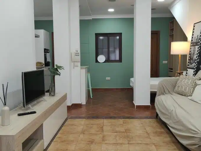 Studio living area with beige sofa, light TV unit and bed at the back – studio for rent, Estepona town centre (ref. AL012B)