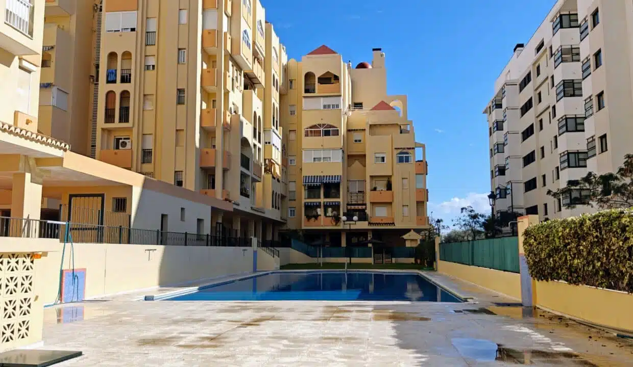 Ochre apartment buildings around a swimming pool, hedge and blue sky – apartment for rent, Estepona town centre
