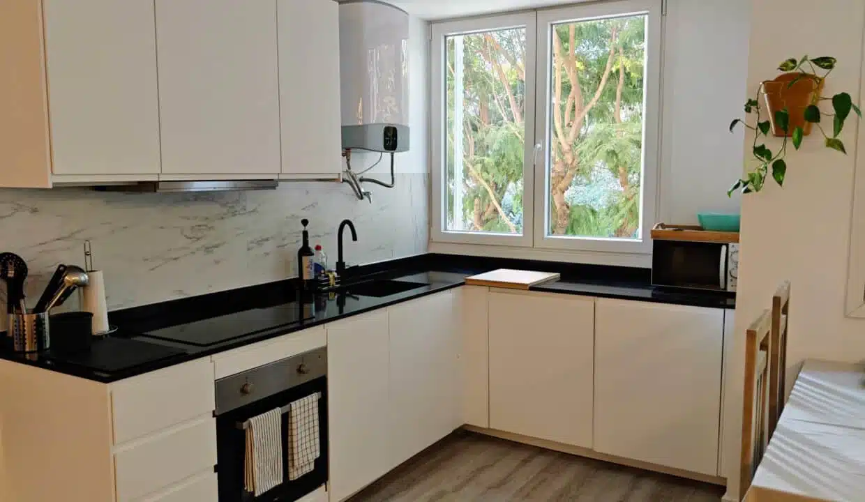 White kitchen with black worktop, oven and windows onto trees – apartment for rent, Estepona town centre