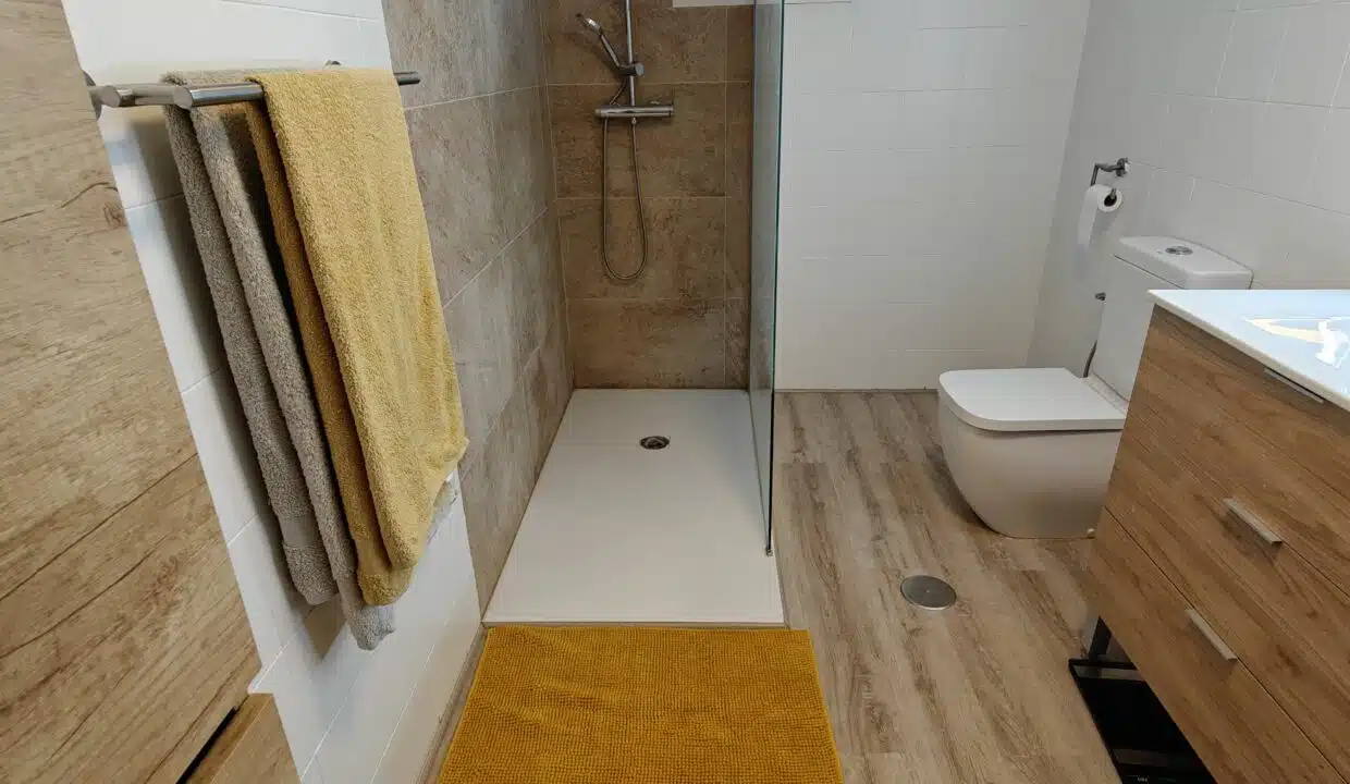 Bathroom with glass-screen shower, yellow towels and wooden vanity unit – apartment for rent, Estepona town centre