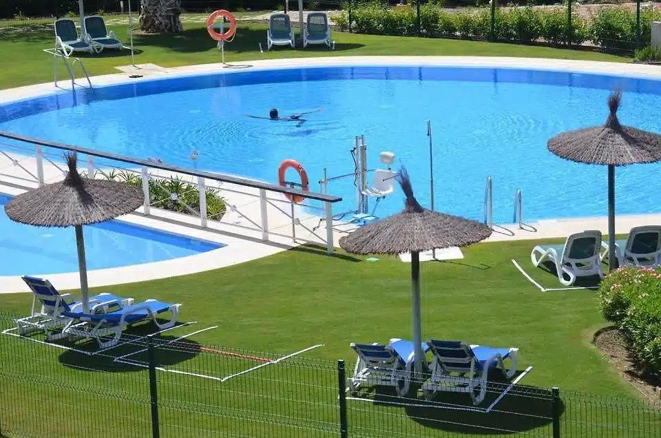 Piscine avec parasols en paille, transats bleus et pelouse – appartement à louer, Parque Botanico, Benahavís (réf. AL035)