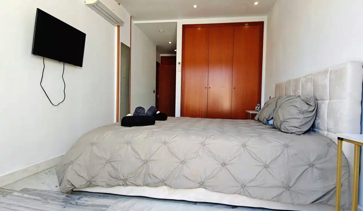 Chambre au lit gris matelassé, TV murale et armoire en bois – appartement à louer, Parque Botanico, Benahavís (réf. AL035)