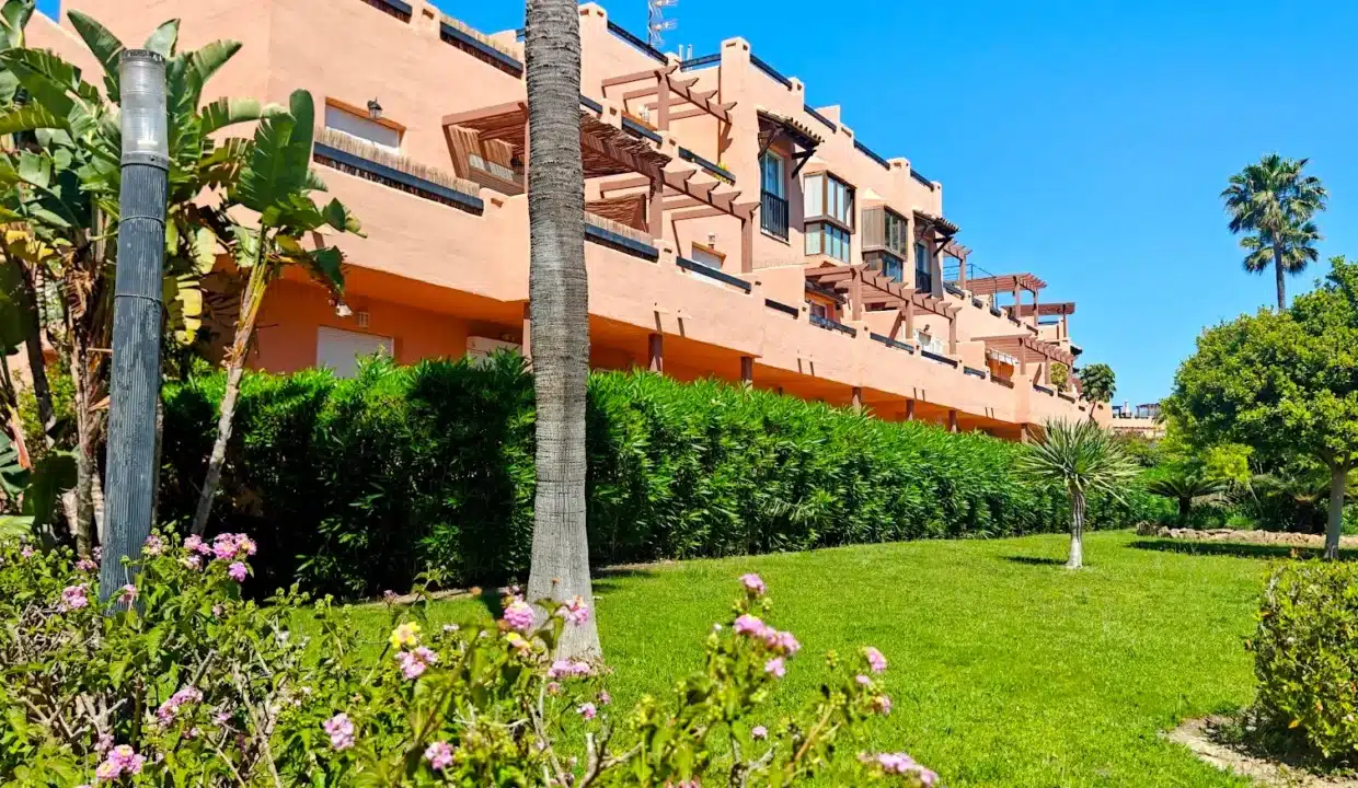 Fachada naranja de la residencia con césped, setos, palmeras – ático en alquiler, Casares del Sol, Casares (ref. AL013)