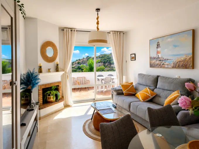 Living room with grey sofa, mustard cushions, brick fireplace – apartment for rent, Casares Real, Casares (ref. SUM003)
