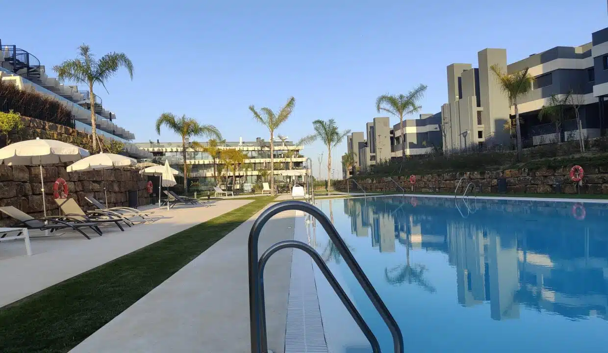 Piscine bordée de transats, parasols et palmiers, immeubles modernes – appartement à louer, Oasis 325, Estepona (réf. SUM038)