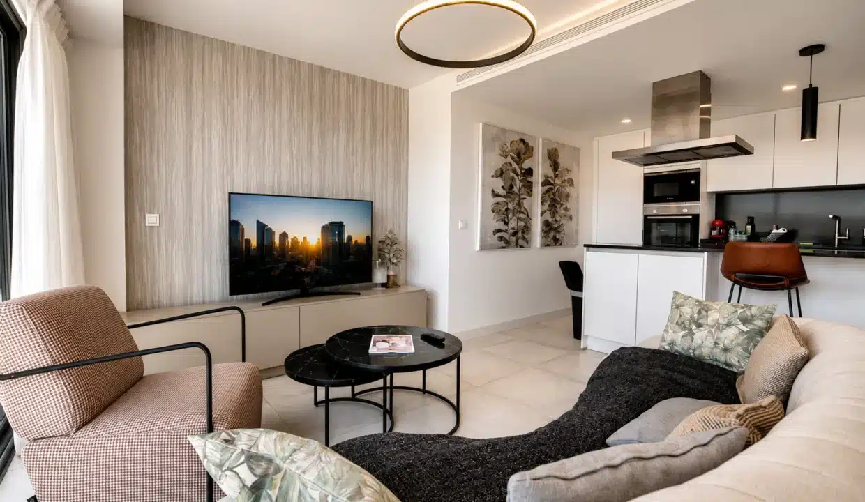 Salon avec canapé crème, tables rondes noires et cuisine ouverte – appartement à louer, Oasis 325, Estepona (réf. AL038)