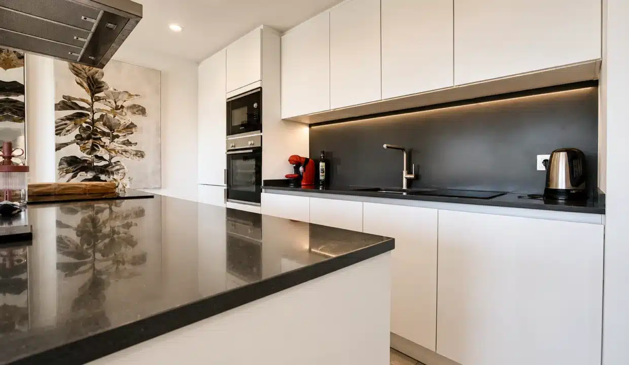Cuisine moderne blanche avec îlot à plan noir, four encastré et hotte – appartement à louer, Oasis 325, Estepona (réf. AL038)
