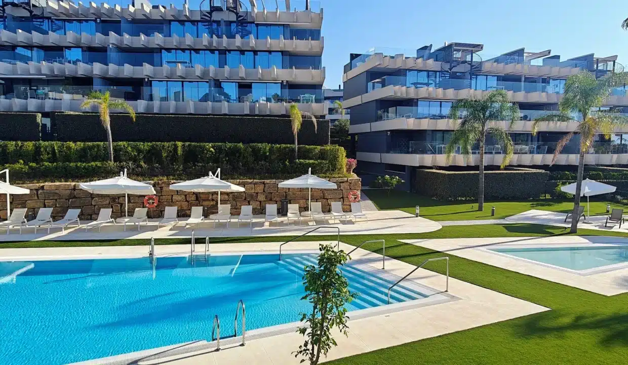 Piscine avec transats blancs devant deux immeubles modernes – appartement à louer, Oasis 325, Estepona (réf. AL038)