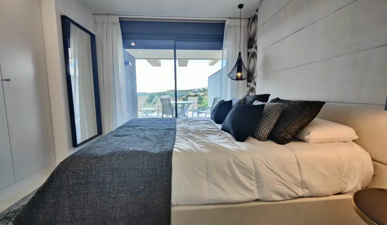 Chambre au lit blanc et coussins bleu marine, baie vers la terrasse – appartement à louer, Oasis 325, Estepona (réf. SUM038)
