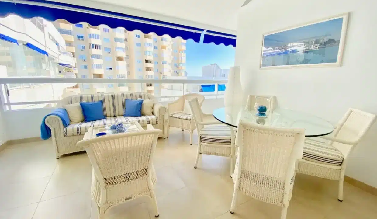 Terrasse couverte avec canapé en rotin, coussins bleus et table en verre – appartement à louer, port d'Estepona (réf. AL051)