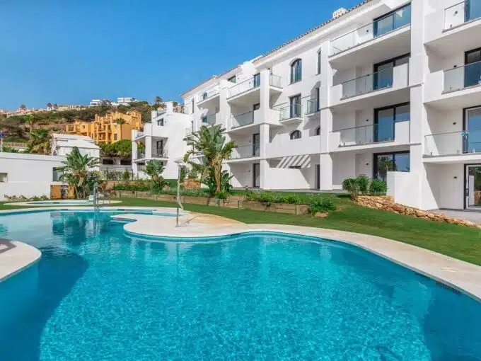 Free-form pool in front of a white building with glass balconies and lawn – apartment for rent, Paloma, Manilva (ref. AL054)
