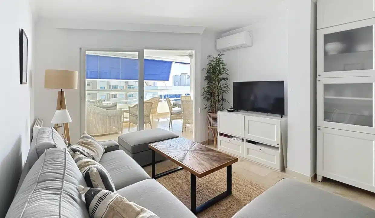 Salon avec canapé gris, table basse en bois et baie vitrée sur le balcon – appartement à louer, port d'Estepona (réf. AL051)