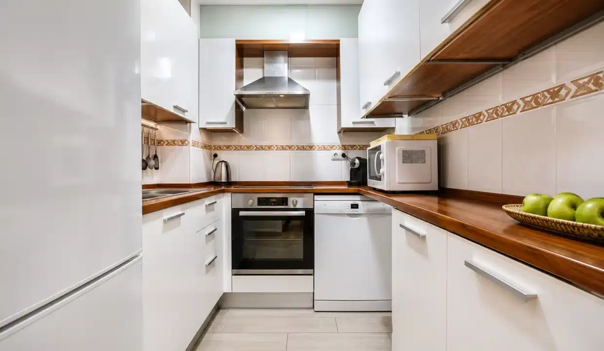 Cuisine en couloir aux placards blancs, plan de travail en bois et four – appartement à louer, port d'Estepona (réf. AL051)
